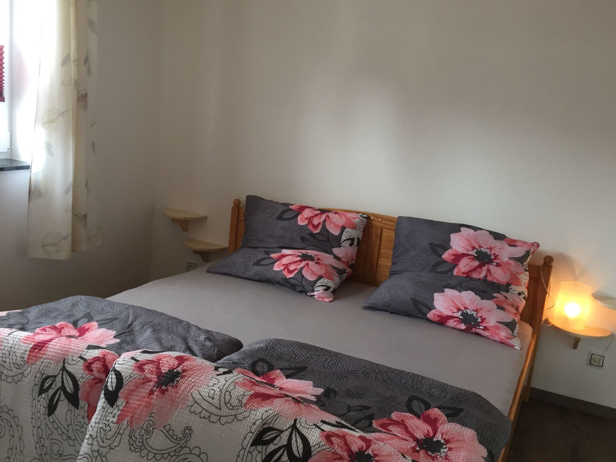 Ein Bett mit blumigem Bettzeug, ein Nachttisch und eine Wandlampe.