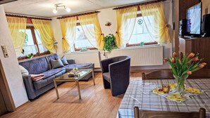A cozy living area with a sofa, a coffee table, a dining table with a placemat, and a TV on a stand. - Vacation home Ziller by Interhome (Crottendorf)