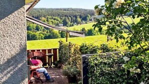 A patio with a view of a green field and trees, a person reading, and a hammock. - Vacation home Ziller by Interhome (Crottendorf)