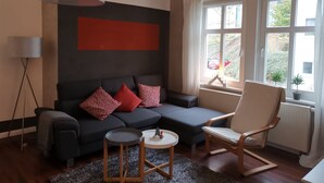 Ein modernes Wohnzimmer mit einem dunklen Sofa, roten Kissen, einem runden Couchtisch und einem Holzstuhl.