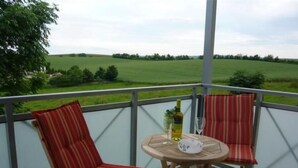 A balcony with two striped chairs and a small round table with a bottle and glass. - in Witzelroda mit Grill und Garten by Interhome (Moorgrund)