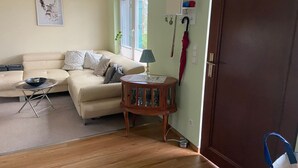 A living room with a beige sofa, a small round table with a lamp, a wooden side table, and a door with a blue handle.