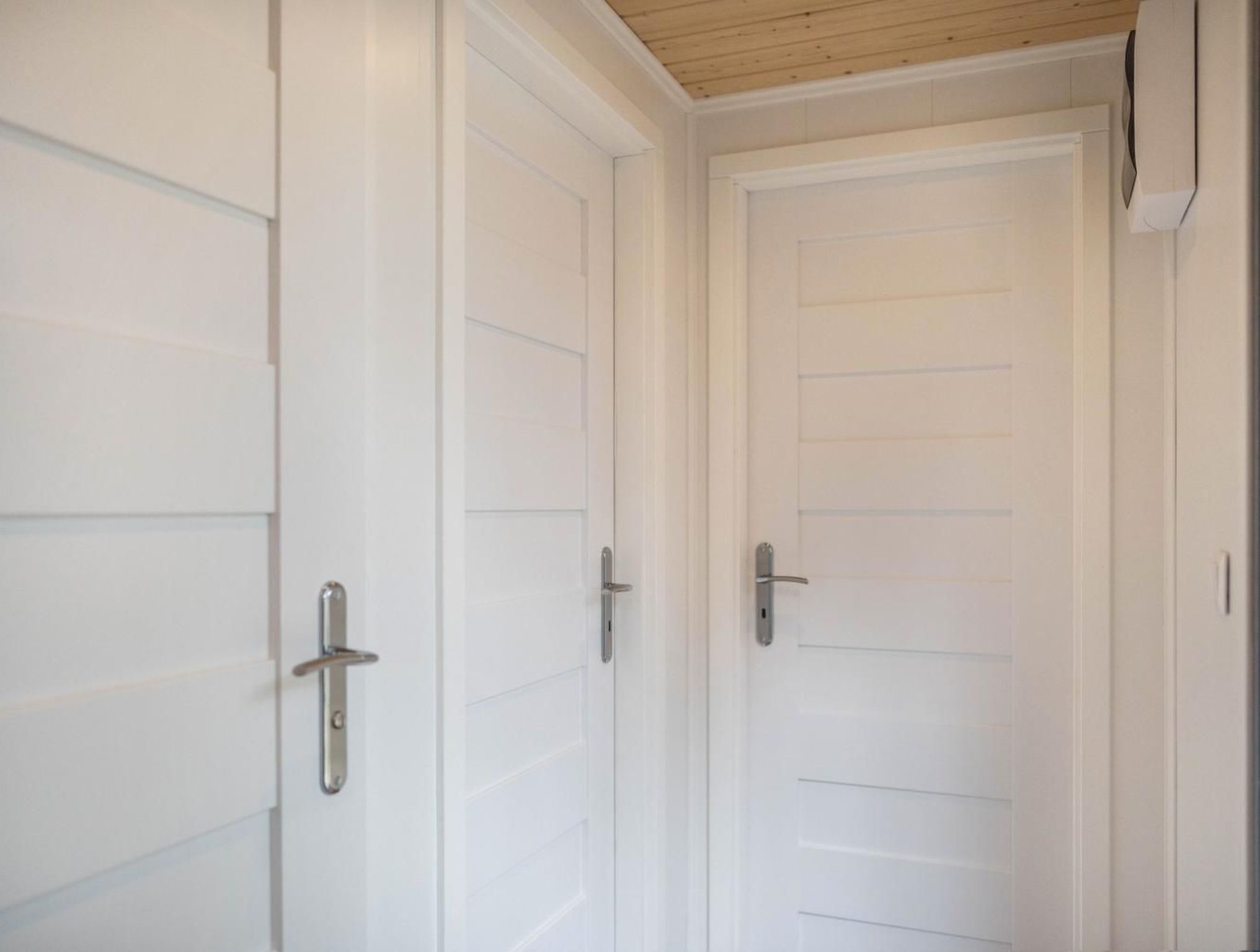 A hallway with white doors, each with a silver handle.