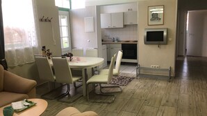 Una sala de estar moderna con un sofá, una mesa de comedor y sillas. Cuenta con una zona de cocina con armarios y un televisor.
