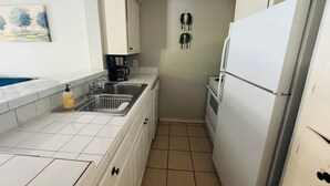 Pieni, käytännöllinen keittiö, jossa on valkoiset kaapit, pesuallas, kahvinkeitin ja jääkaappi.
