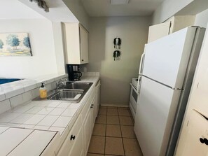 A compact kitchen with white cabinets, a sink, a coffee maker, and a refrigerator.