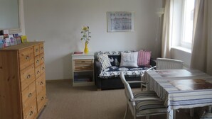 A cozy room with a wooden dresser, a sofa with patterned cushions, a small table with a striped tablecloth, and a window with curtains. - Appartement in Wismar mit Garten by Interhome (Wismar)