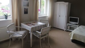 A bedroom with a bed, a TV, a wardrobe, a dining table with chairs, and a window with curtains. - Appartement in Wismar mit Garten by Interhome (Wismar)
