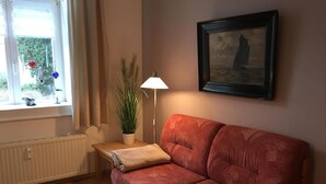 A cozy living room with a red sofa, a small table with a lamp, a potted plant, and a framed picture on the wall. - Appartement in Wismar mit Terrasse und Garten by Interhome (Wismar)