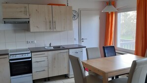 A compact kitchen with a stove, sink, and cabinets. There is a dining table with chairs and a window with curtains. - Familienfreundliche Wohnung in Vorland mit Garten by Interhome (Grimmen)