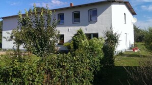 A two-story white house with a flat roof, surrounded by greenery and a clear blue sky. - Familienfreundliche Wohnung in Vorland mit Garten by Interhome (Grimmen)