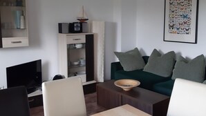 A living room with a dark green sofa, striped pillows, a wooden coffee table, and a framed butterfly artwork on the wall. - Familienfreundliche Wohnung in Vorland mit Garten by Interhome (Grimmen)