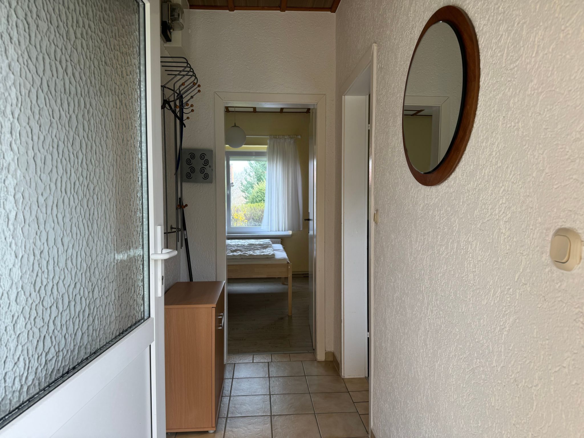 A narrow hallway with a wooden cabinet, a mirror, and a window with curtains.