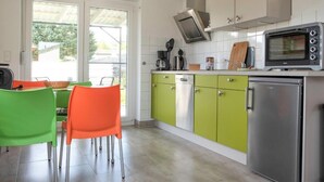 Eine moderne Küche mit grünen und weißen Schränken, einem Edelstahlkühlschrank, einem eingebauten Backofen und einem Fenster mit Blick auf einen Garten.