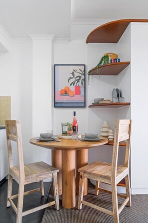 Un comedor con una mesa redonda de madera y dos sillas de madera. Encima de la mesa, hay un cuadro enmarcado en la pared.