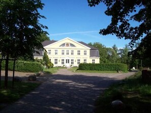 Um edifício grande, de dois andares, com fachada simétrica, entrada central e um jardim formal à frente.