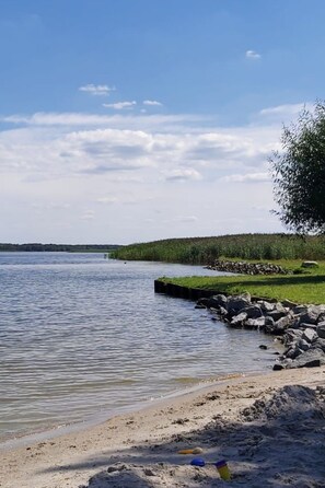 A beach with a calm lake, a grassy area, and a rocky shoreline. - gemütlicher Bungalow by Interhome (Altwarp)