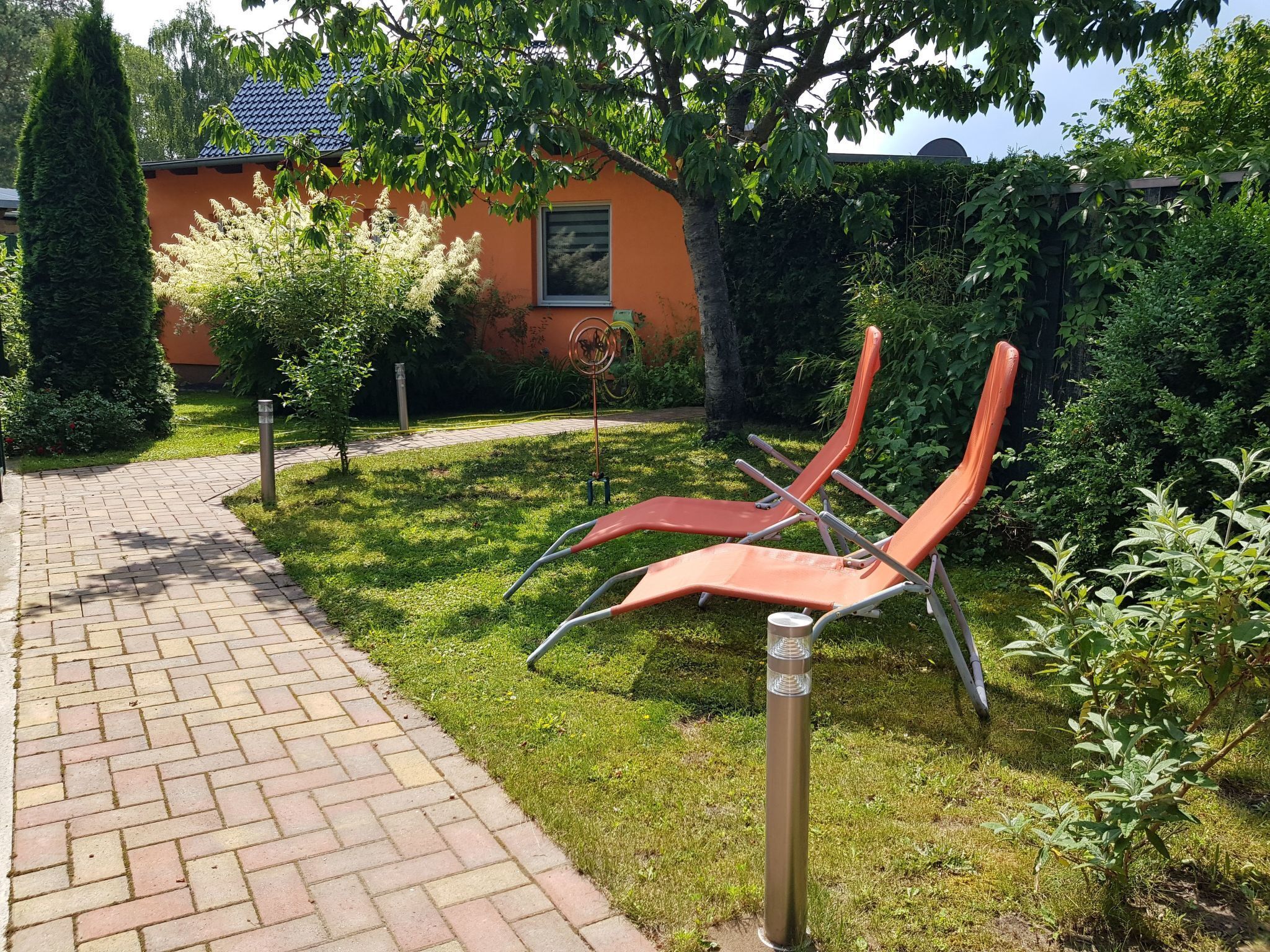 Ein Garten mit einem gepflasterten Weg, zwei orangefarbenen Liegestühlen und einem Gebäude mit blauem Dach.