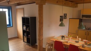 A cozy kitchen with wooden beams, a dining table with chairs, a bookshelf, and a window. - Holunderhof by Interhome (Altwarp)