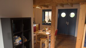 A cozy room with a wooden floor, a bookshelf, a dining table with chairs, and a window with a view of greenery. - Holunderhof by Interhome (Altwarp)