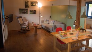 A cozy living room with a wooden floor, a sofa, a rocking chair, a dining table with chairs, and a lamp. - Holunderhof by Interhome (Altwarp)
