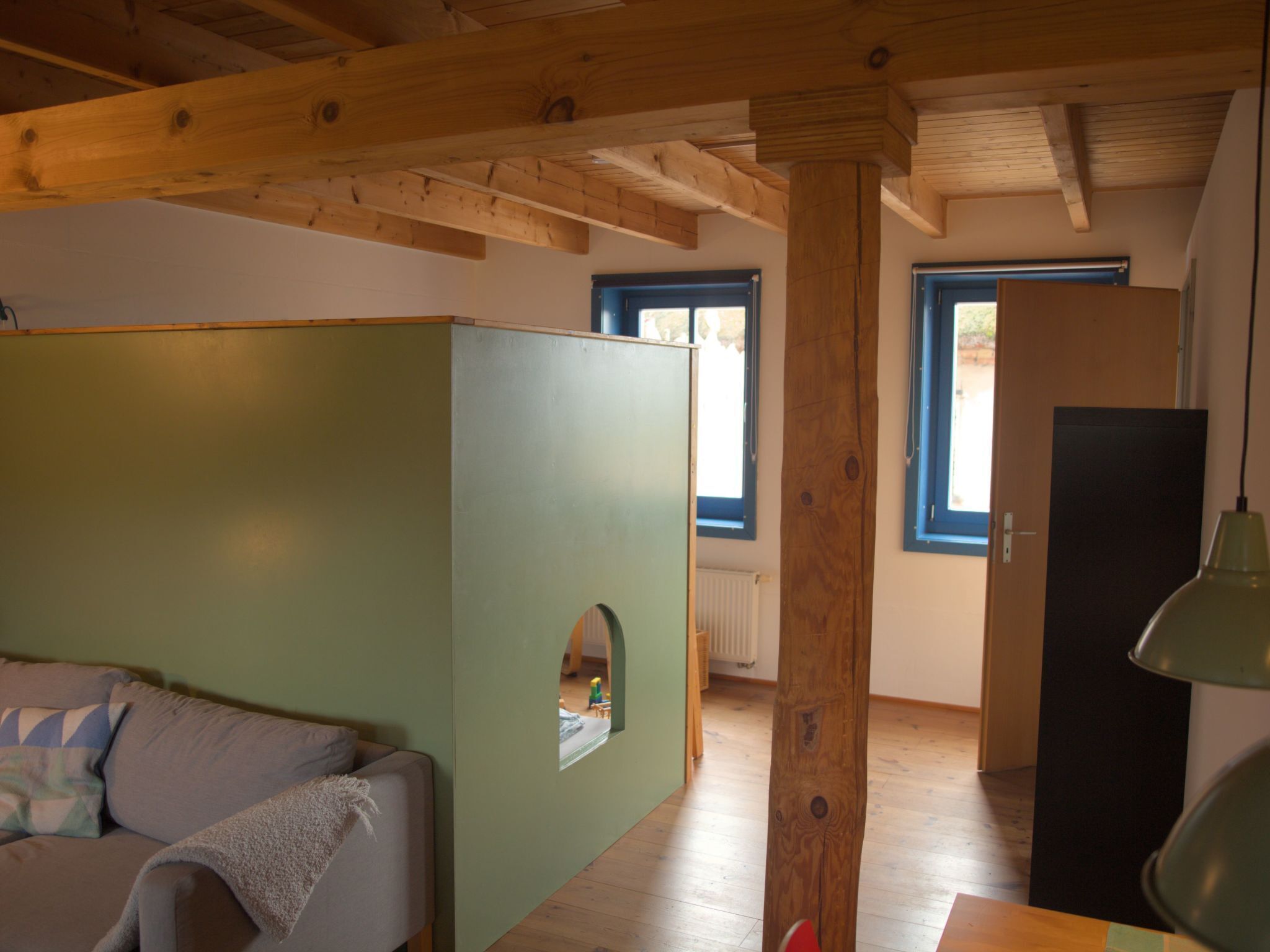 A room with a wooden ceiling, a green partition, a sofa, a door, and a window.