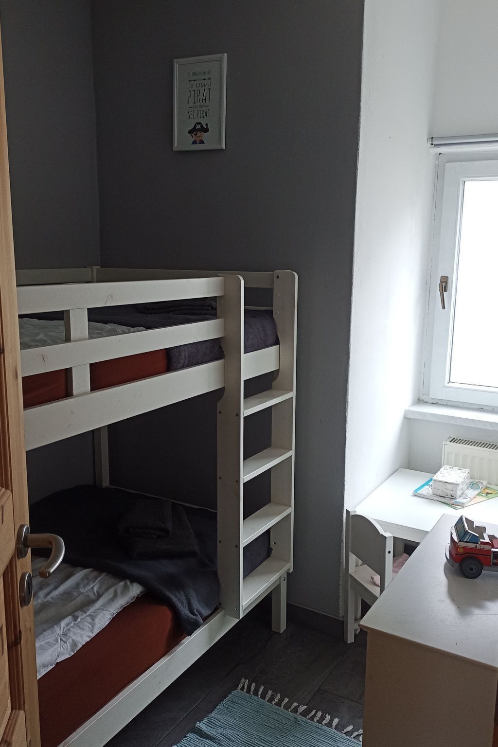 Un lit superposé avec un bureau et une chaise, un radiateur et un tableau encadré au mur.