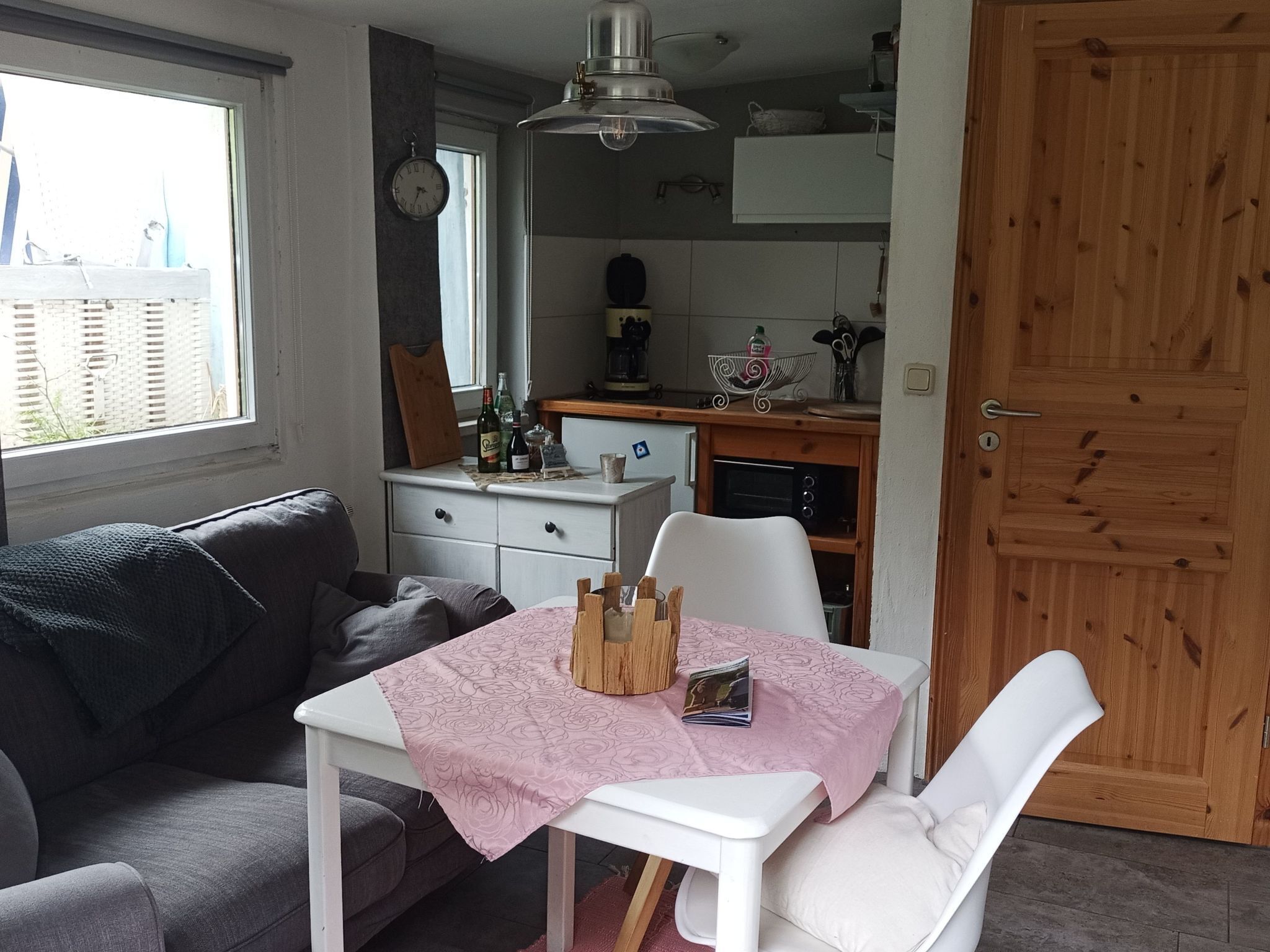 Un ambiente compatto con un tavolo da pranzo, un divano, angolo cottura completo di fornello e forno, e una porta in legno.