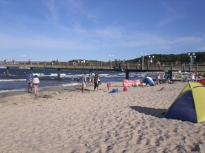 A beach with a wooden pier, people walking, and a tent set up on the sand. - Modernisiertes Haus zwischen Stralsund und Barth by Interhome (Karnin)