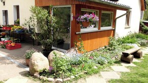 A small wooden building with a tiled roof, a flower basket hanging by the window, and a garden with various plants and flowers. - Schiemann by Interhome (Karnin)