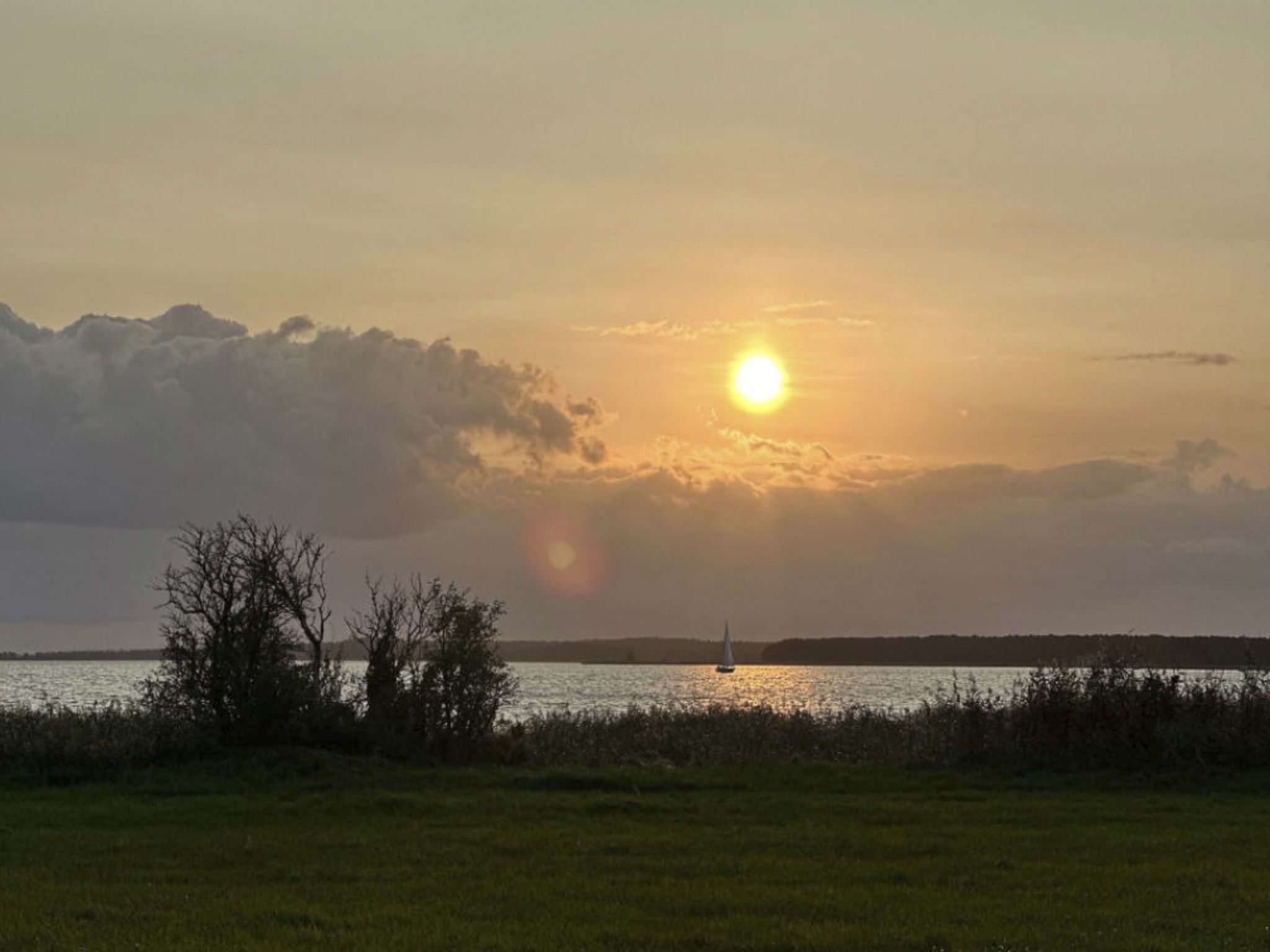 A sunset over a body of water with a sailboat.