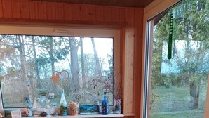A cozy wooden room with a cushioned bench, a window with a view of trees, and a small bird statue on the windowsill. - Schiemann by Interhome (Karnin)