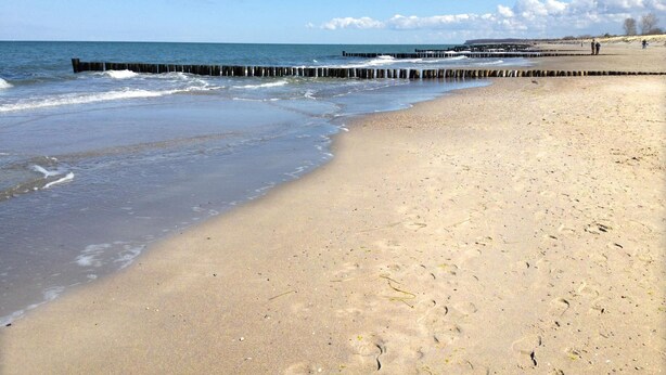 Ein sandiger Strand mit einem hölzernen Steg, der sich ins Wasser erstreckt.