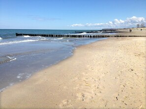 En sandstrand med en träbrygga som sträcker sig ut i vattnet.