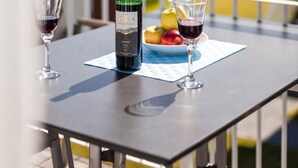 Ein Balkon mit Tisch für zwei Personen, ausgestattet mit einer Weinflasche, zwei Gläsern und einer Obstplatte.