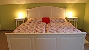 Un lit recouvert d’une couvre-lit à motifs floraux, deux tables de chevet avec des lampes et un mur vert.