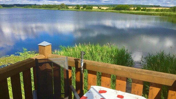 Une terrasse en bois avec une table et une chaise, donnant sur un lac paisible, le tout entouré de verdure.