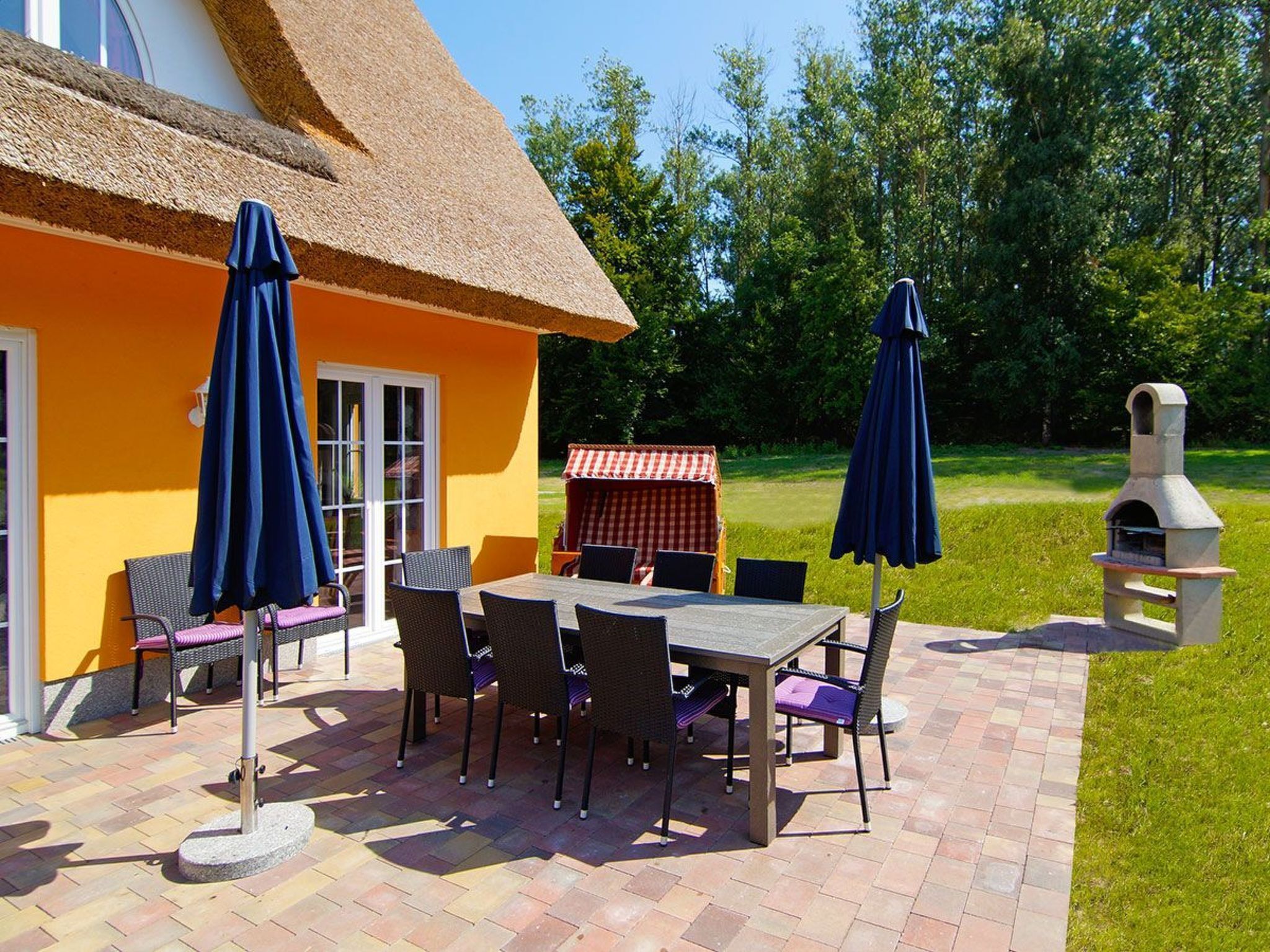 Eine Terrasse im Freien mit Tisch, Stühlen, einem Grill und Sonnenschirmen.