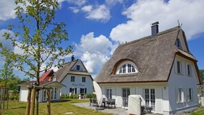 Ein traditionelles Reetdachhaus mit weißer Fassade, einem sichtbaren Schild mit der Aufschrift 'Haas Rony' und einer Terrasse mit Gartenmöbeln.