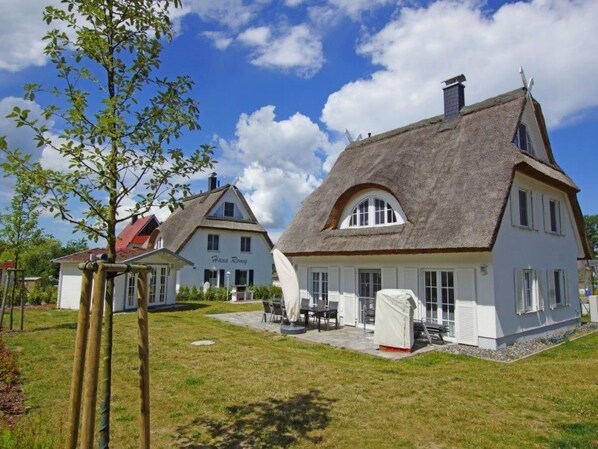 Ein traditionelles Reetdachhaus mit weißer Fassade, einem sichtbaren Schild mit der Aufschrift 'Haas Rony' und einer Terrasse mit Gartenmöbeln.