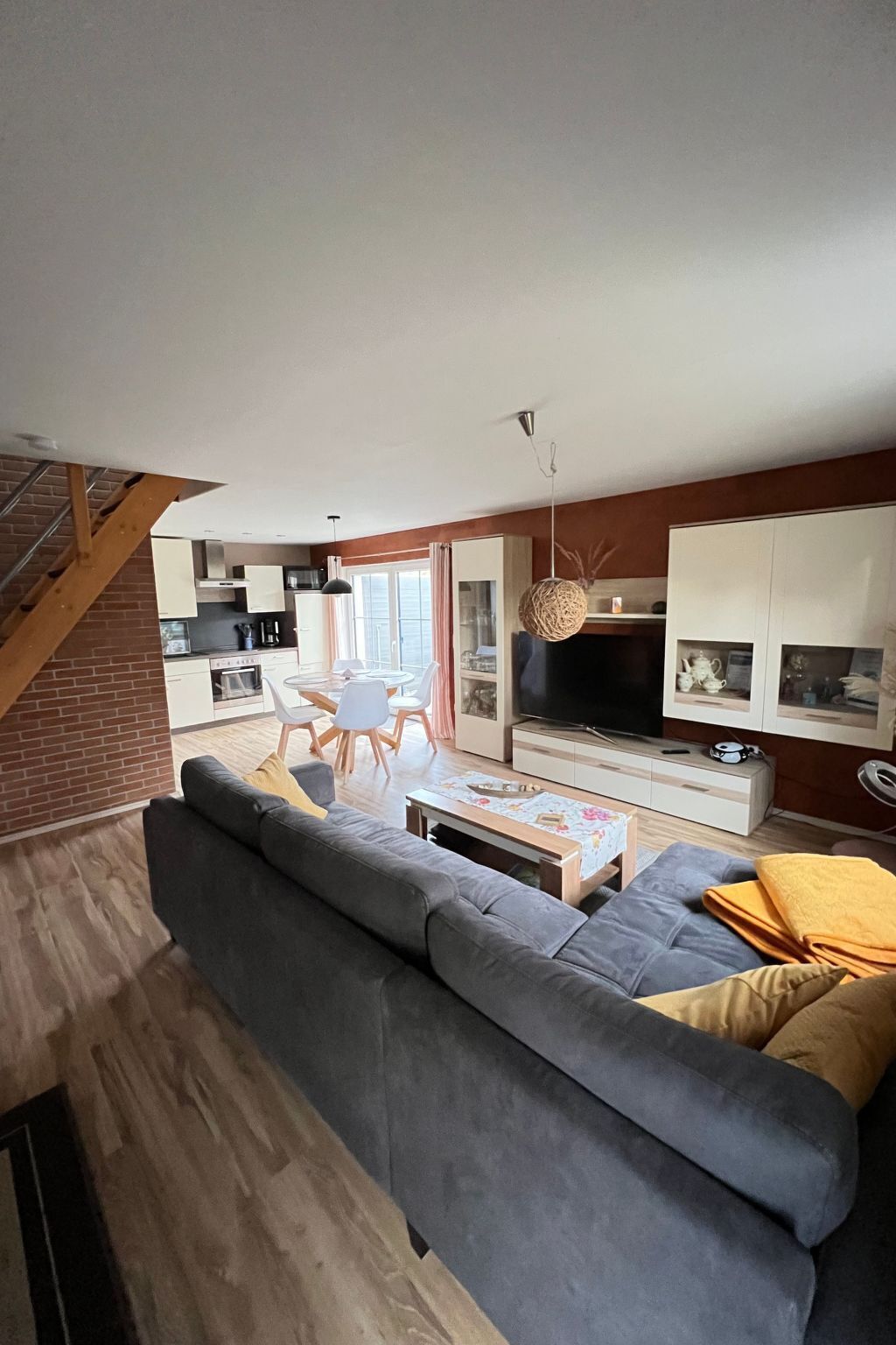 Een moderne woonkamer met een grijze bank, een eethoek met witte stoelen, een televisie en een trap.