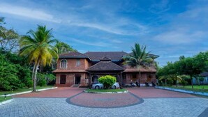 Una casa grande de ladrillo con tejado de baldosas, rodeada de palmeras y un camino de entrada pavimentado.