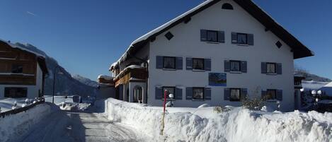 Ein mehrstöckiges Gebäude mit geneigtem Dach, großen Fenstern und einer schneebedeckten Fassade.