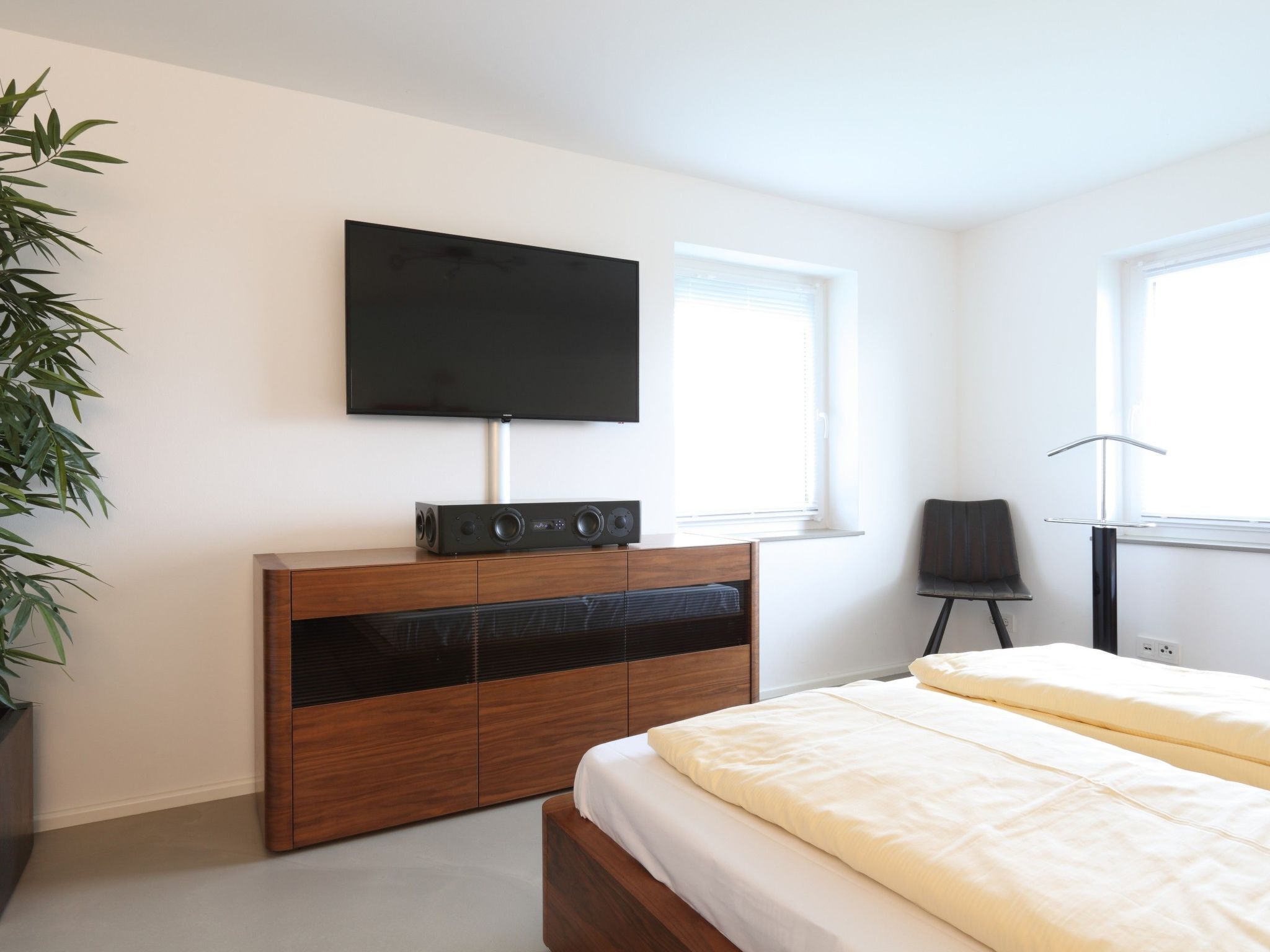 Quarto moderno com uma cama, televisão na parede, um armário de madeira e uma cadeira.