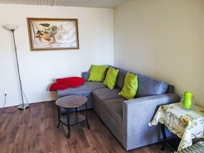Ein Wohnzimmer mit grauem Sofa, einem kleinen runden Tisch, einer Stehlampe und einem gerahmten Bild an der Wand.