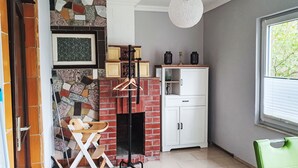 Une pièce avec une cheminée, une armoire blanche, un fauteuil vert et un luminaire suspendu.