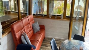 Ein Zimmer mit einem roten Ledersofa, einem Esstisch mit Stühlen und großen Fenstern mit Blick ins Freie.