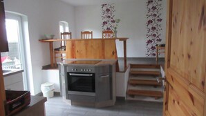 A compact kitchen with a built-in oven, wooden cabinets, and a small dining area with a chair and table.
