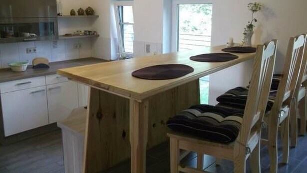 A kitchen with a wooden table and chairs, a refrigerator, and a window with curtains.