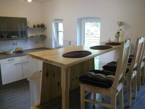 A kitchen with a wooden table and chairs, a refrigerator, and a window with curtains.